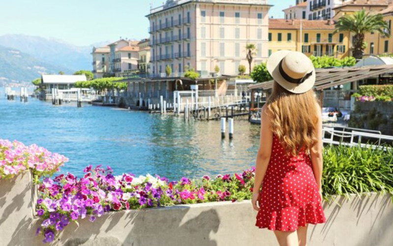 Woman in a red dress and sun hat admiring a scenic waterfront in Italy